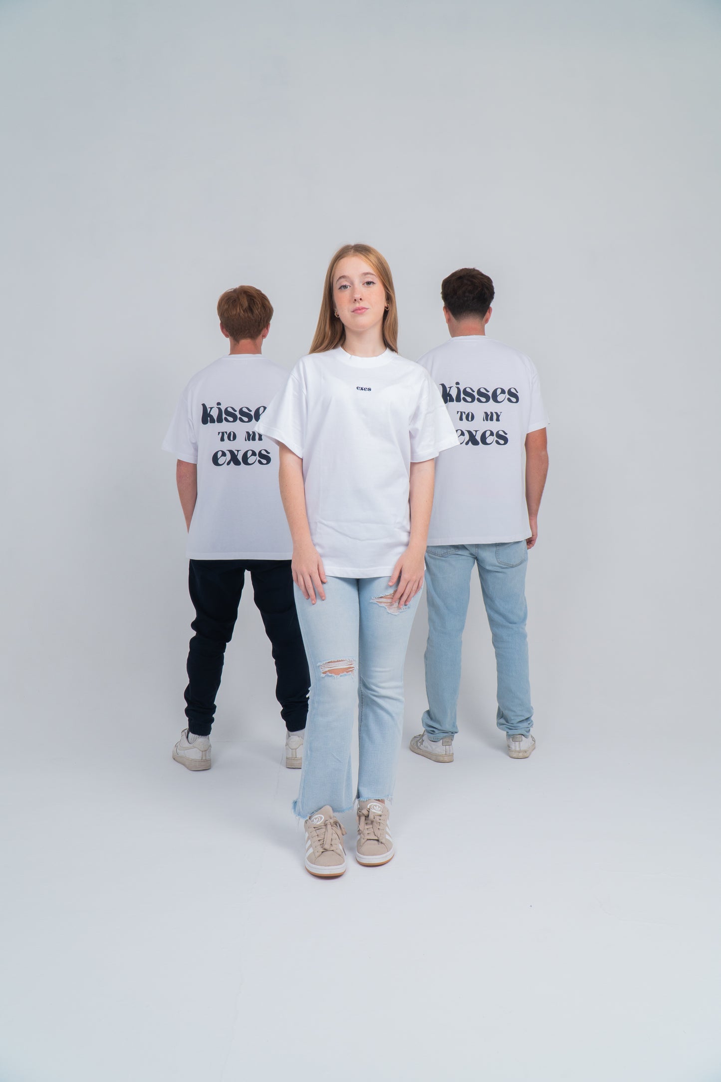 Dos chicos de espaldas uno a cada lado y en medio una chica de cara. Llevan la camiseta blanca con el diseño en la espalda de "kisses to my exes". Y en el pecho está el logo bordado de exes en azul ocuro. 