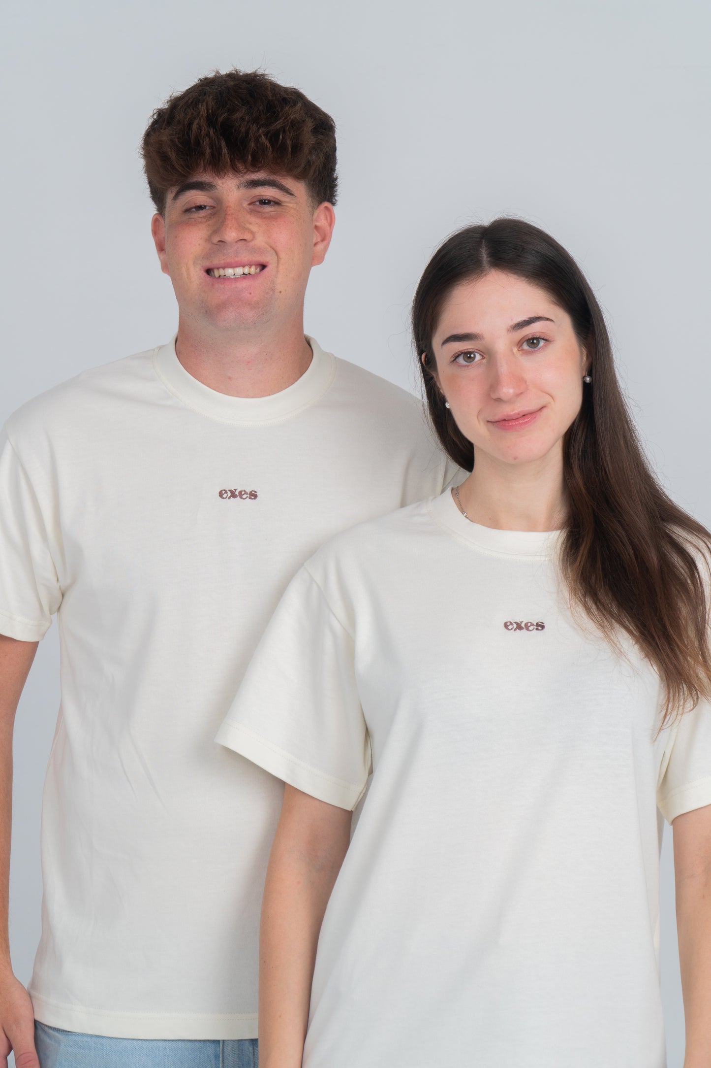 Chico y chica vistiendo camiseta/tee beige con logo bordado de la marca exes.