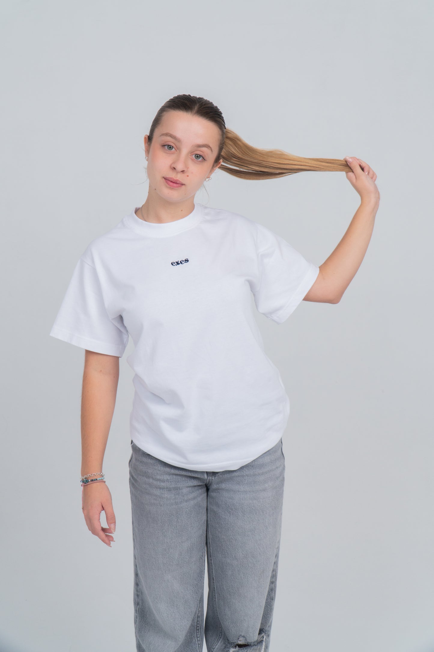 Chica de frente lleva la camiseta blanca con el logo bordado de exes en azul.