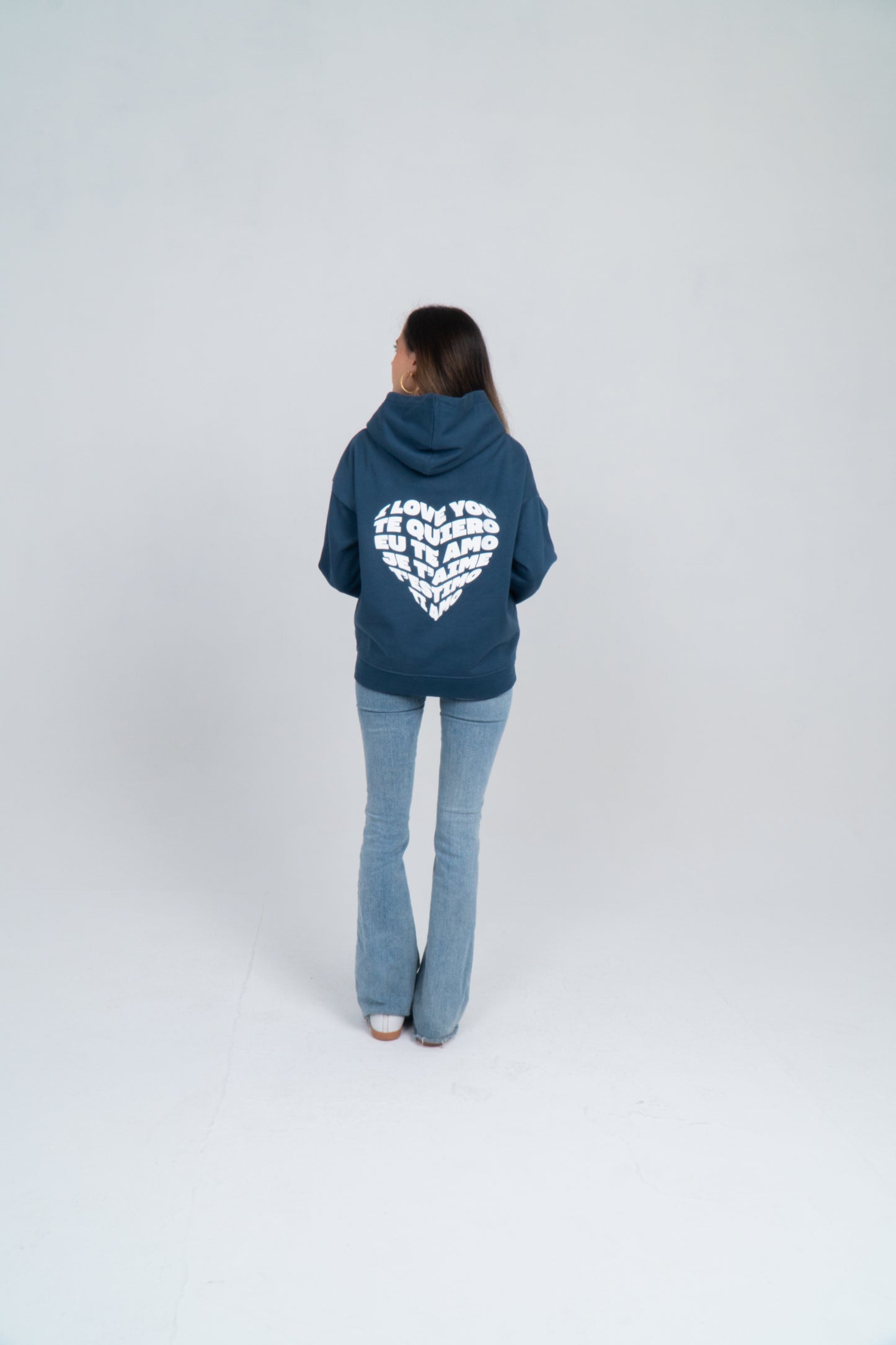 Chica de espaldas. En la espalda de la sudadera azul se muestra el diseño de un corazón formado por la palabra te quiero en diferentes idiomas. El orden es: i love you, te quiero, eu te amo, je t'aime, t'estimo, ti amo. 